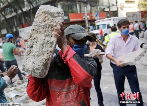 墨西哥城的一處倒塌的建筑廢墟旁，志愿者徒手搬走石塊,，以方便救援行動(dòng)展開(kāi),。