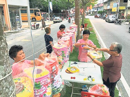 村民分工合作將透明的塑料袋倒套著紙制的燈籠，避免燈籠被雨淋濕或被曝曬損壞,。（馬來西亞《中國報》/村民提供照片）