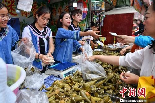 中國(guó)僑網(wǎng)資料圖:6月5日,商販身穿少數(shù)民族服飾售賣特色粽子。中新社記者 任東 攝