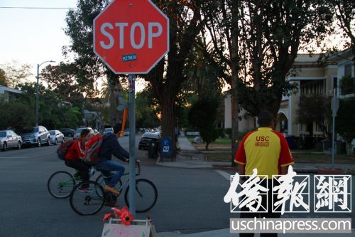 2名中國留學(xué)生騎車在“小黃衣”旁邊經(jīng)過,。(美國《僑報》/周慧一