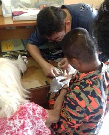 中國僑網(wǎng)消拯官員正在仔細(xì)地為華裔年長婦女剪戒指,。(馬來西亞《星洲日報》)
