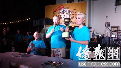 中國僑網黃恩恩(右)巾幗不讓須眉,,1分鐘吃了22個餃子,,擊敗男性PK對手,獲得吃餃子大賽的冠軍,,她捧著獎杯,,眼眶濕潤,。(僑報記者高睿攝)