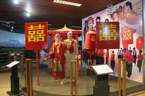 中國僑網(wǎng)文化廳展出華人傳統(tǒng)婚禮模型似是而非,,解說版上說明新人身穿紅色喜衣,,但新郎卻穿米黃色衣服,背景圖案也稍感格格不入,。(馬來西亞《星洲日報》)