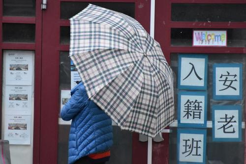 中國僑網(wǎng)日前,,葉女士冒雨撐傘等待警崗開門,。(美國《世界日報》/李秀蘭 攝)