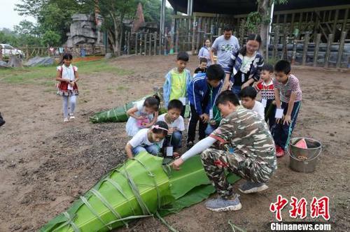 中國僑網(wǎng)圖為飼養(yǎng)員與小朋友一起給非洲象包粽子?!№n璐 攝