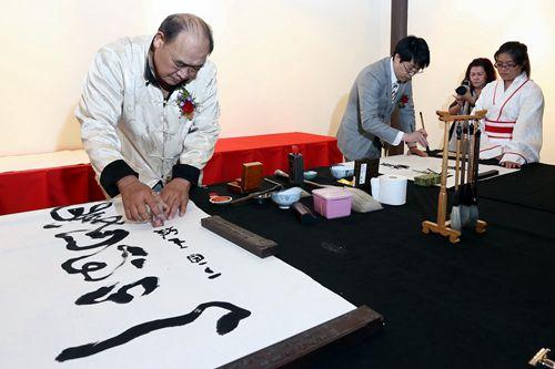 中國僑網馬來西亞書藝協會會長王雅(左)在完成作品后蓋上姓名印章,,于樂(右)專注揮毫。(馬來西亞《星洲日報》)