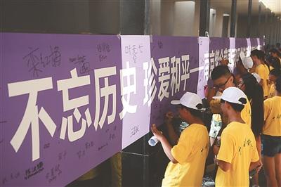 中國(guó)僑網(wǎng)圖為華裔青少年在“不忘歷史 珍愛和平”橫幅上簽名,。新華報(bào)業(yè)視覺中心記者 萬程鵬 實(shí)習(xí)生 陳儼 攝