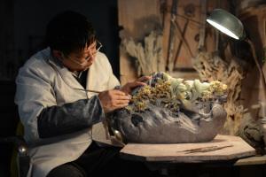 中國僑網(wǎng)非物質文化遺產項目代表性傳承人、省級工藝美術大師杜小亮在使用雕刀修細作品