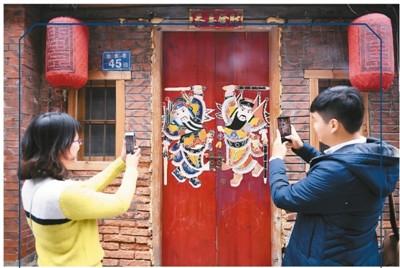 中國僑網(wǎng)圖為兩名游人在金魚巷拍攝閩南傳統(tǒng)民居大門上的門神圖案,。 新華社記者 林善傳攝
