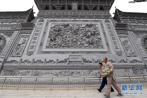 10月16日,沈占偉(右)從他和徒弟們歷時(shí)兩年,、精雕細(xì)刻數(shù)千塊青磚組合而成的九龍壁下走過,。新華社記者
