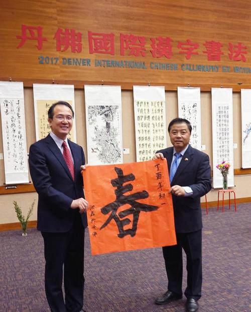 中國僑網(wǎng)洪磊總領(lǐng)事(左)寫“春”字請屠新時會長向丹佛華人問候,。
