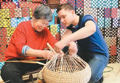 中國僑網(wǎng)圖為4月15日,,來自摩爾多瓦的比契爾(右)在農(nóng)民梁春梅(左)指導(dǎo)下體驗草柳編工藝品編織技藝,。(陳彬 攝)