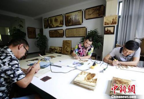 中國(guó)僑網(wǎng)鄧師華(中)和他的團(tuán)隊(duì)用烙鐵繪制張家界山水畫,。 吳勇兵 攝